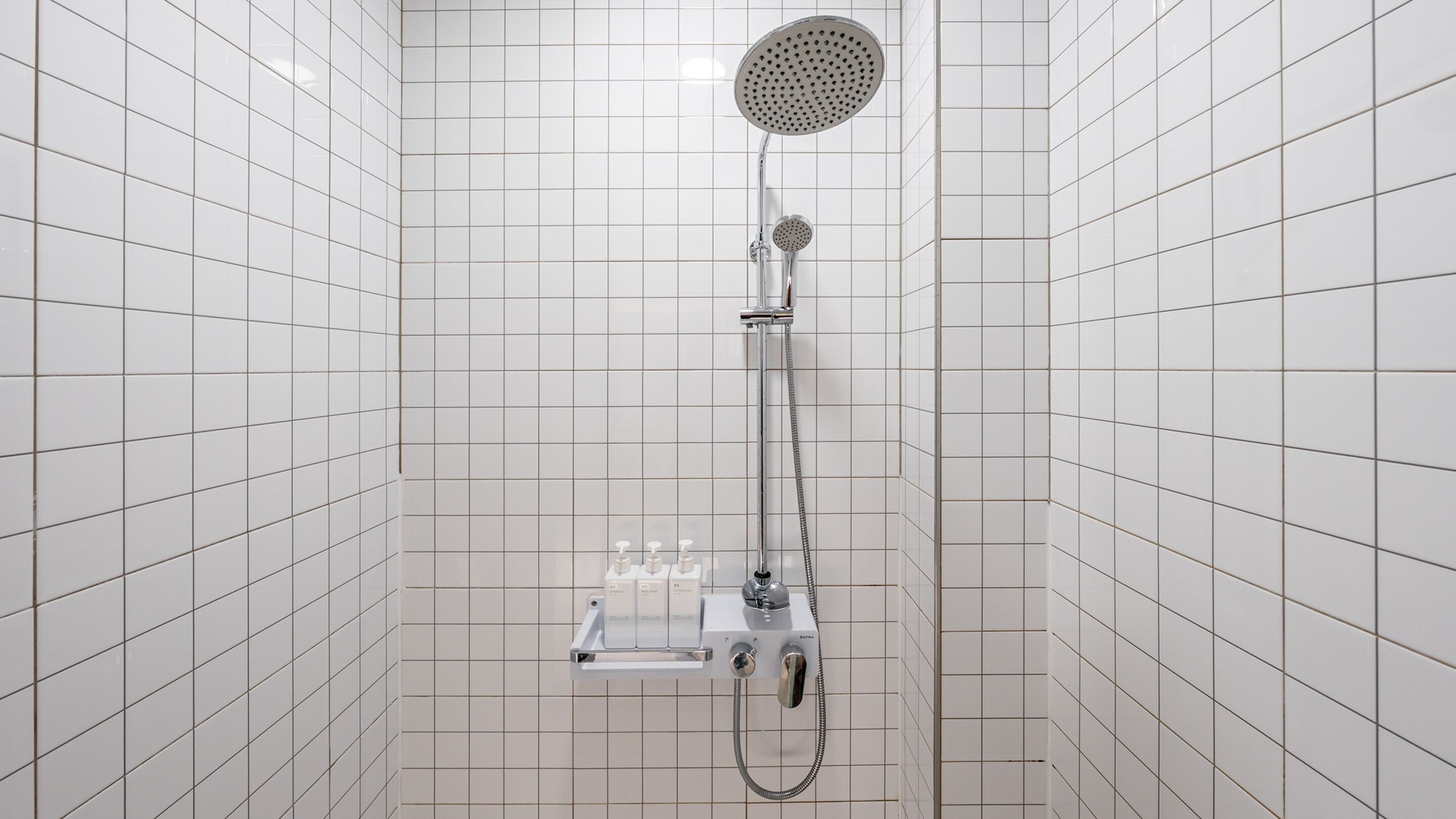 A shower with a handheld showerhead and a fixed showerhead, both mounted on a wall.