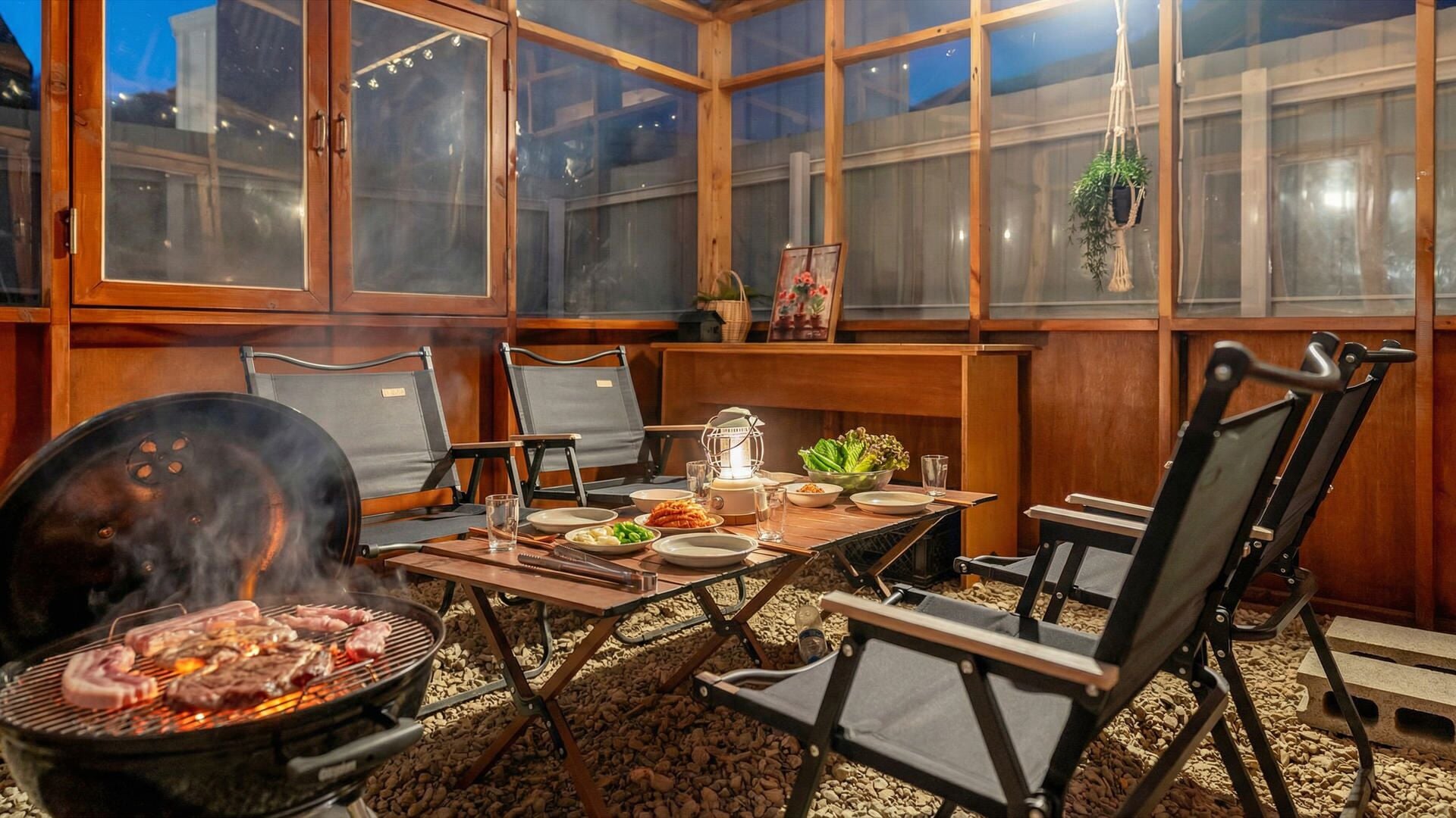 En terrasse med grill, spisebord, stole og udsigt gennem store vinduer.