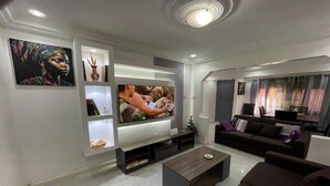 Uma sala de estar moderna com televisão de tela plana, um sofá marrom escuro, uma mesa de centro e um rack para TV com prateleiras.