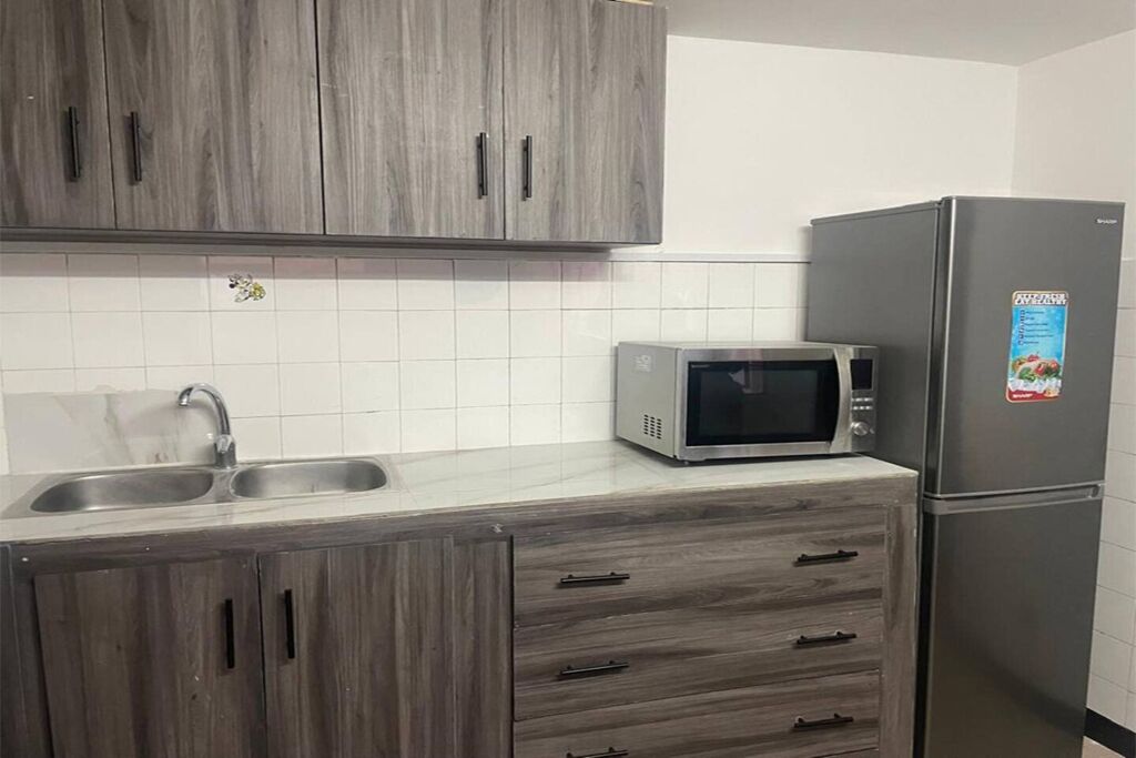 A kitchen with grey cabinets, a stainless steel sink, a microwave, and a refrigerator.