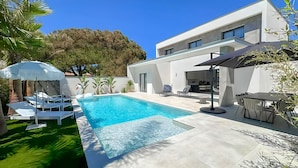 Et moderne hus med swimmingpool, udendørs møbler og en patio.