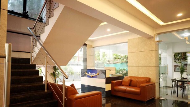 A modern lobby with a staircase, a reception desk, and a seating area with leather sofas. - Saara Residency (Pune)