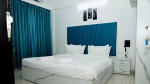 A hotel room with a large bed, a nightstand, and a blue headboard. - Saara Residency (Pune)