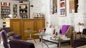 Un salón acogedor con un sofá, sillones y una mesa de centro de vidrio. Se ve un área de cocina con armarios de madera y una barra de bar al fondo.