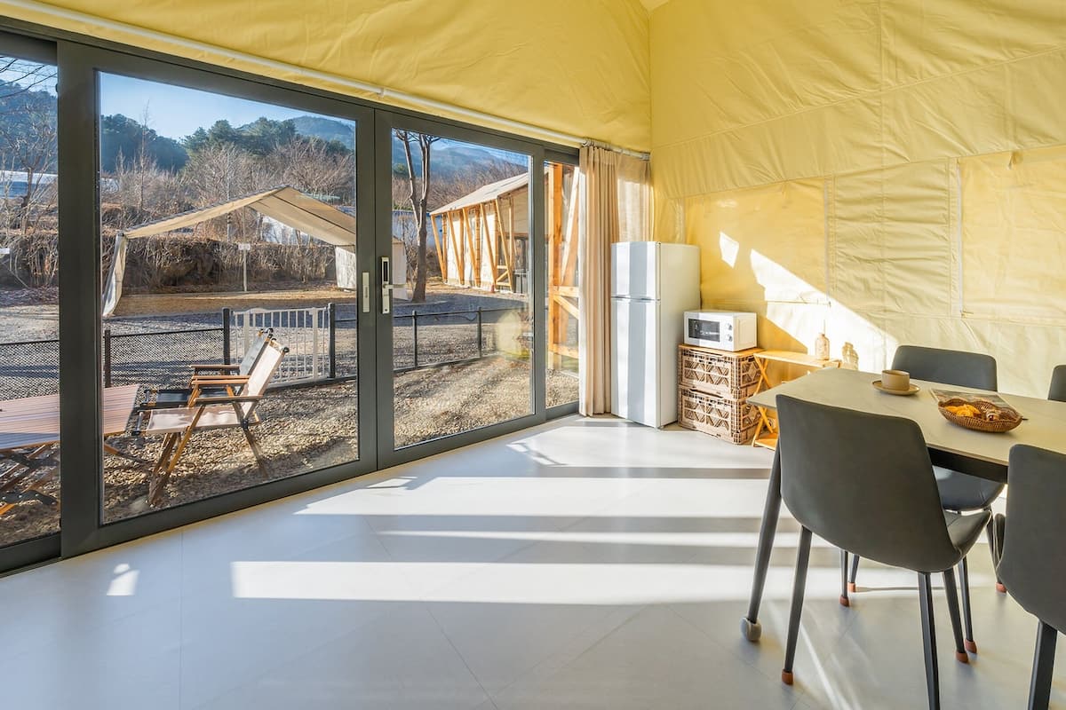 A modern tent-style room with a dining table and chairs, a refrigerator, and a view of the outdoors.