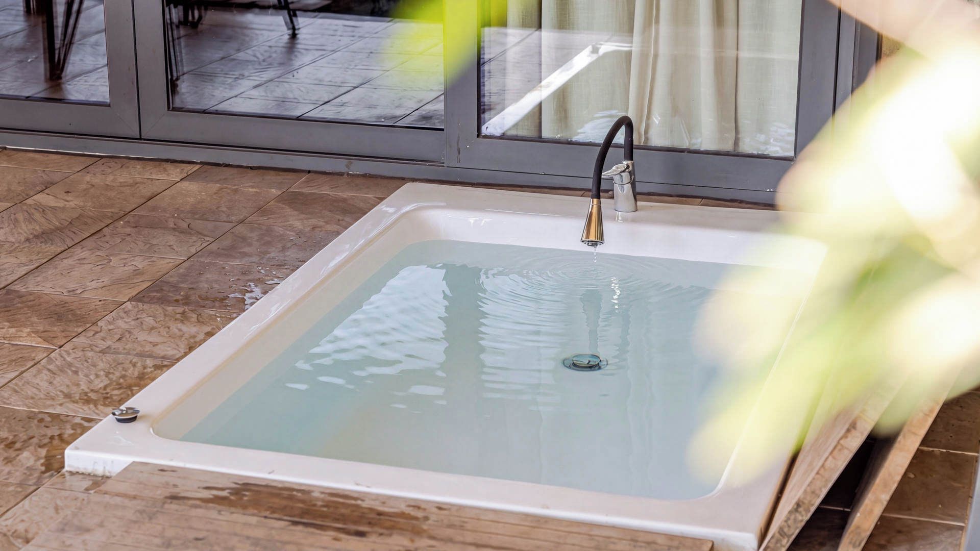 Un baño con una bañera blanca, un grifo y una puerta de cristal que da a una zona con suelo de azulejos.