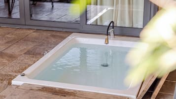 Un baño con una bañera blanca, un grifo y una puerta de cristal que da a una zona con suelo de azulejos.