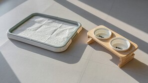 Een huisdiertjesbed en twee kommen op een houten standaard.