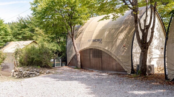 A tented accommodation with a gravel driveway, trees, and a stone wall. - Gapyeong High Mong Glamping & Camping (Gapyeong)