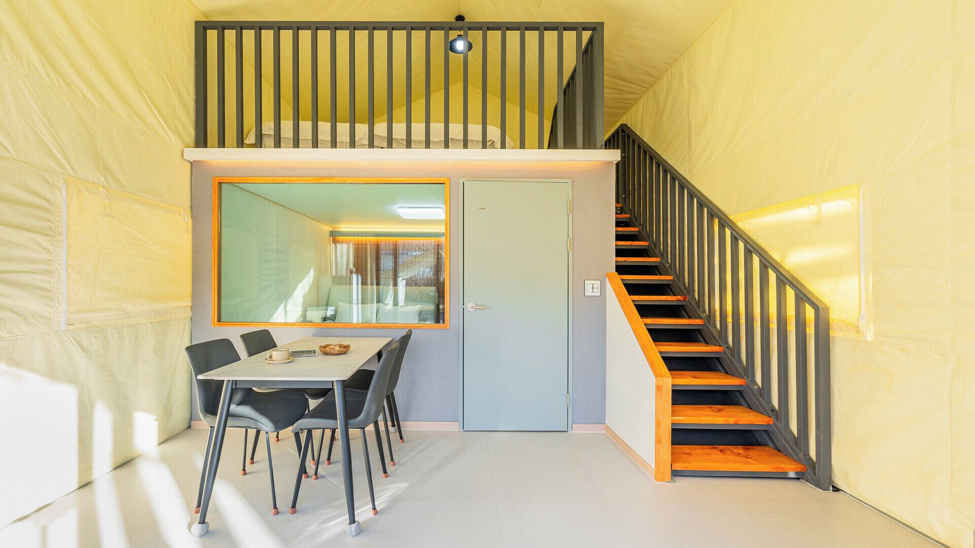 A room with a dining table, chairs, a staircase, and a door.