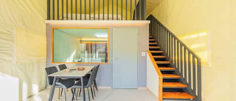 Una habitación con una mesa de comedor, sillas, una escalera y una puerta.