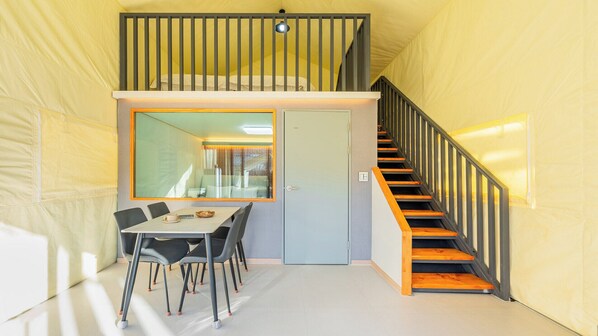Una habitación con una mesa de comedor, sillas, una escalera y una puerta.