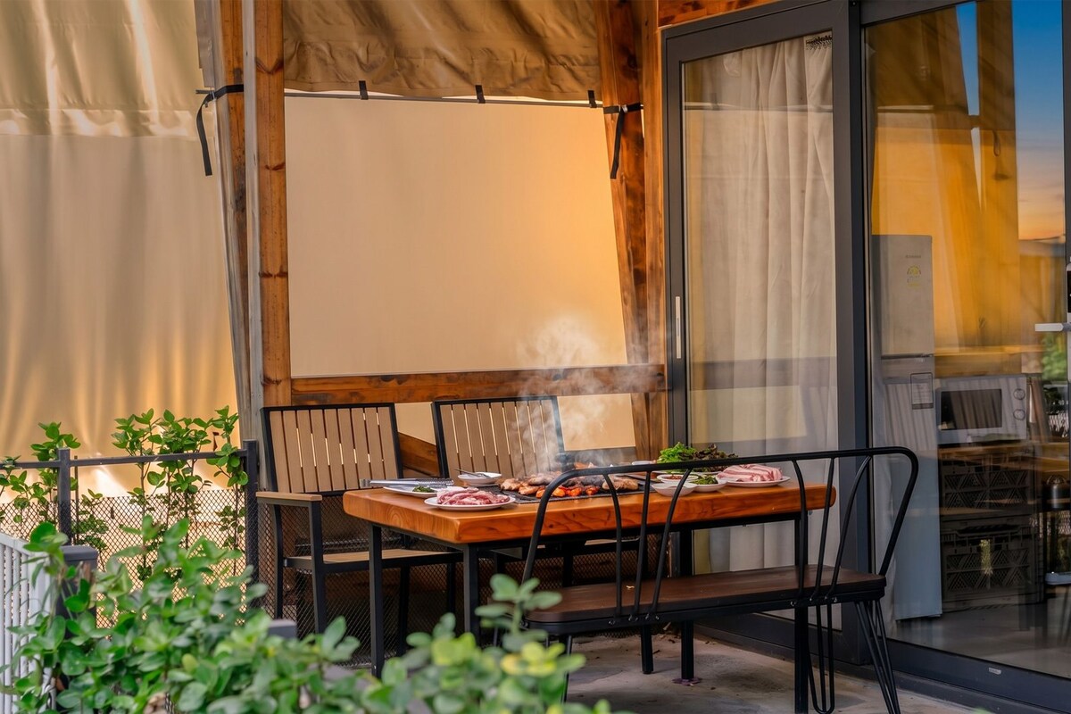 Een buiten eetgedeelte met een tafel voor twee personen, omringd door stoelen, uitzicht op de omgeving en een groot raam.