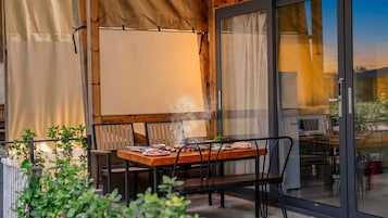 Un espacio de comedor al aire libre con una mesa lista para dos personas, rodeada de sillas, vista al exterior y un ventanal grande.