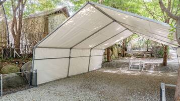 A covered outdoor area with a gravel floor, metal fencing, and trees in the background.