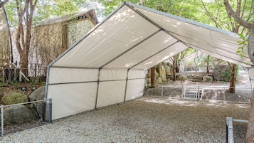 Un espacio al aire libre techado con suelo de grava, cercado de metal y árboles al fondo.