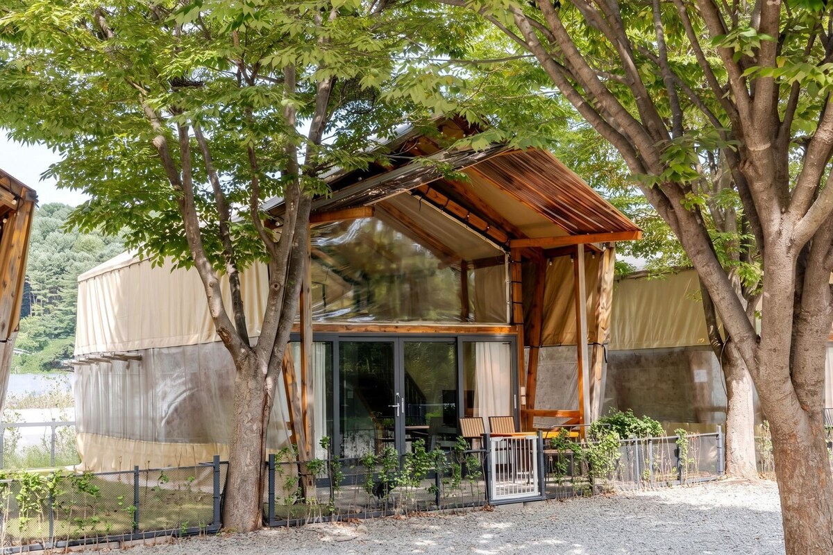 Een houten chalet met een overdekte veranda, grote ramen en een omheinde tuin.