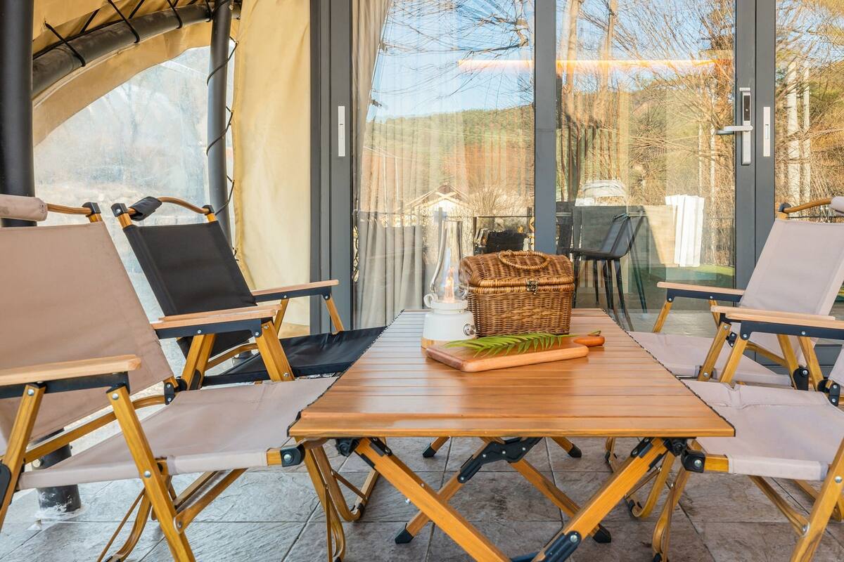 A cozy outdoor seating area with wooden tables and foldable chairs, a wicker basket, and a table lamp.