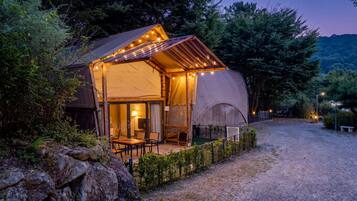Alojamiento con carpa, una zona de estar exterior cubierta, un interior visible con mesa y sillas, y un camino de grava que conduce a la entrada.