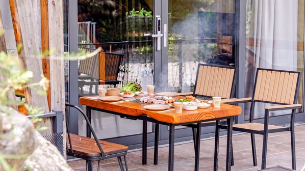 An outdoor dining area with a table set for two, chairs, and a glass door leading to a garden. - Gapyeong High Mong Glamping & Camping (Gapyeong)