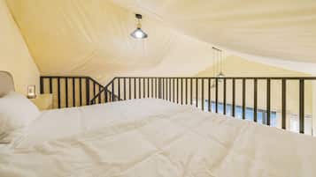 A tented accommodation with a bed, a nightstand, and a hanging light fixture.