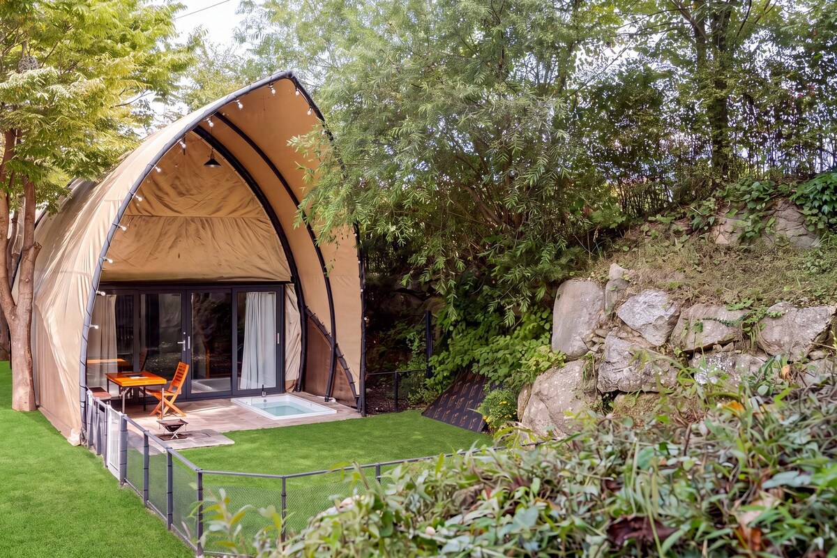 Een tentvormige constructie met een glazen deur en een terras met een tafel en stoelen.