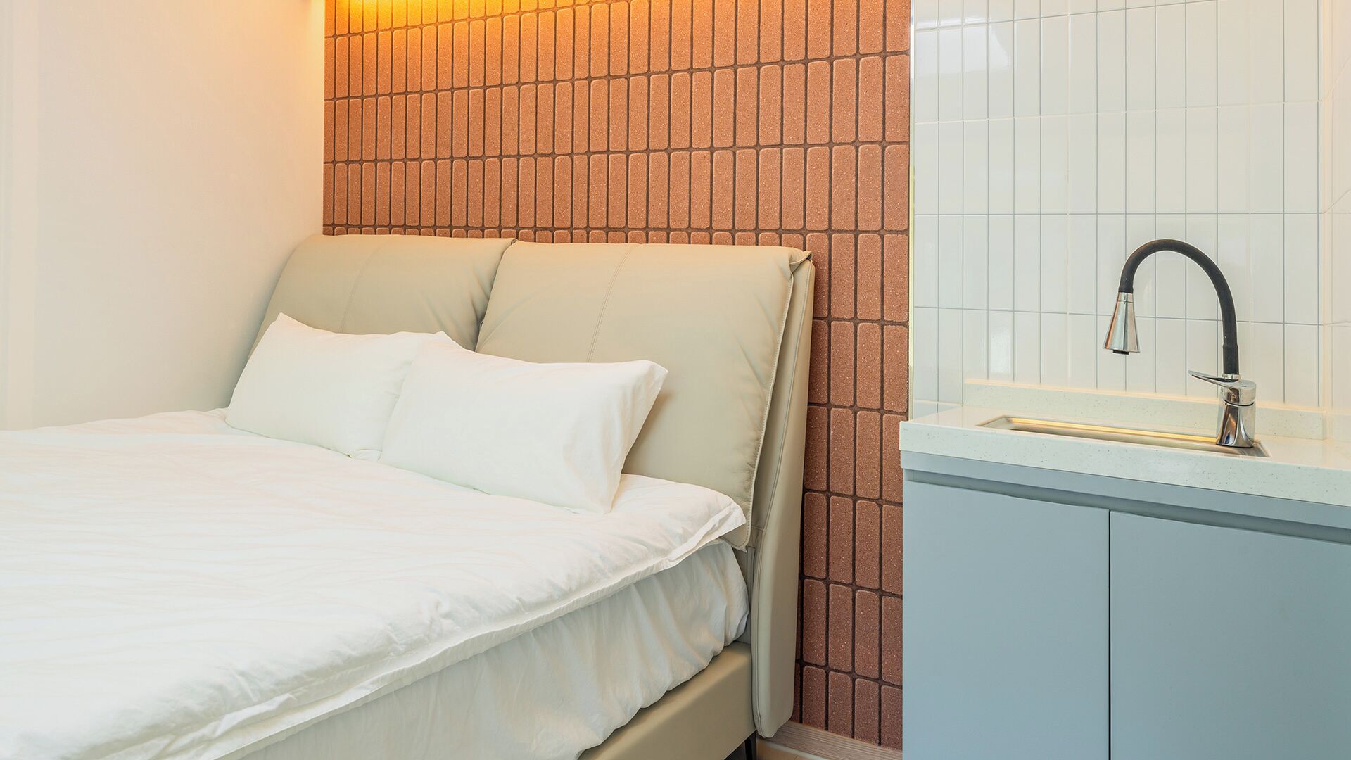 A bedroom with a bed, a nightstand, and a bathroom with a sink and mirror.