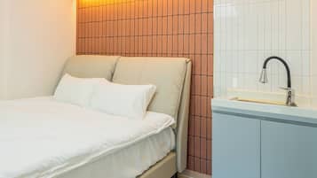 A bedroom with a bed, a nightstand, and a bathroom with a sink and mirror.