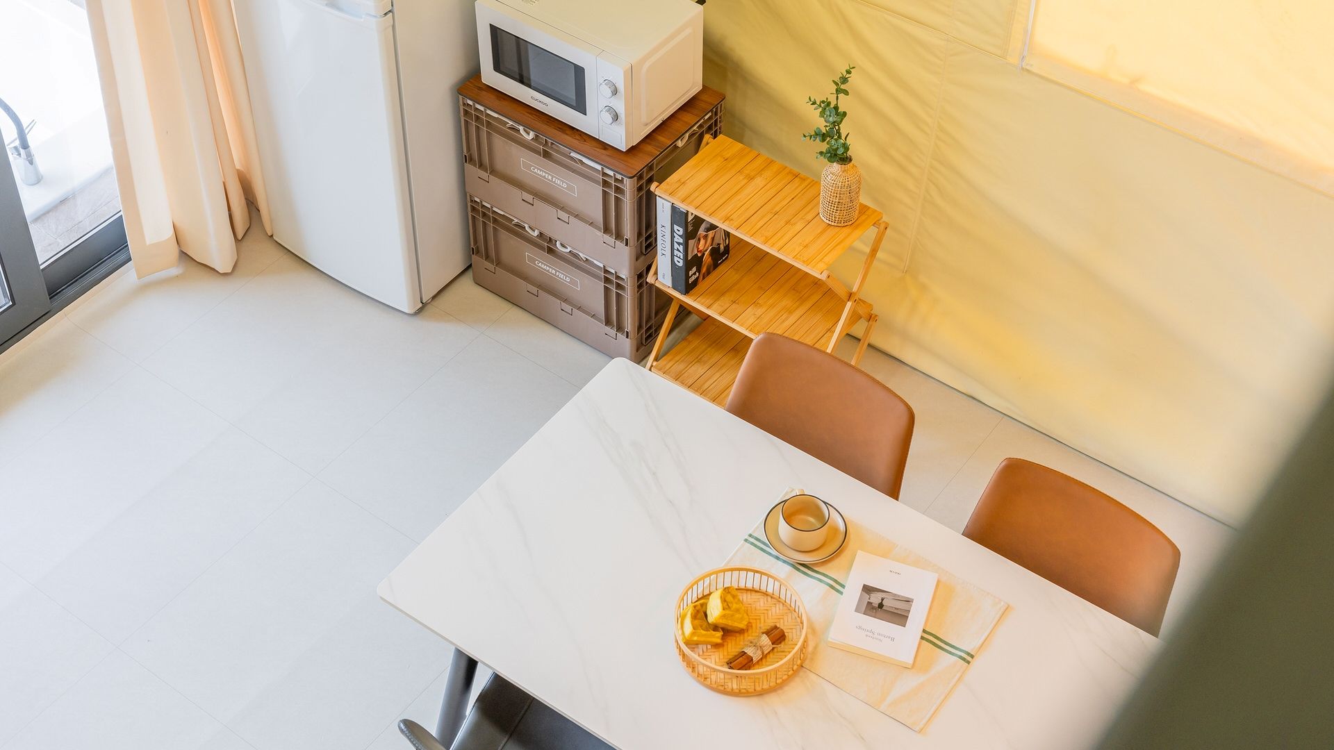 Cocina compacta con microondas, cajones de almacenamiento y una mesa de madera con una cesta de pan y un menú.
