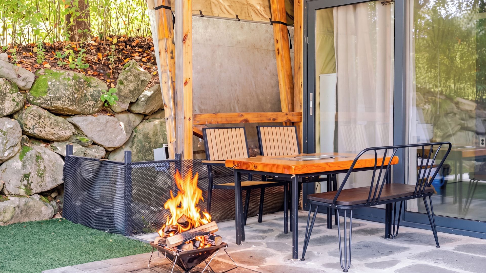 An outdoor seating area with a fire pit, stone wall, and glass door.