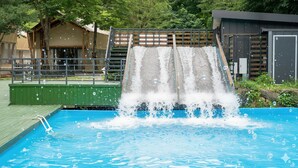 A swimming pool with a waterfall feature, surrounded by a wooden deck and a metal fence.