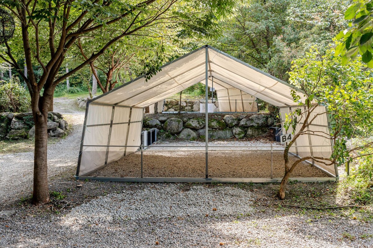 Een overdekt terras met een achtergrond van een stenen muur, omringd door grind en bomen.