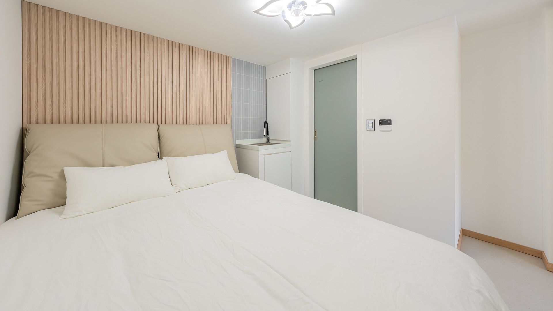 Un dormitorio con cama, mesita de noche, lámpara de pared y una puerta.