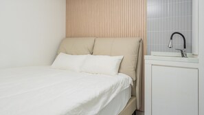 A bed with white bedding and two pillows, a wooden headboard, a white bedside table with a faucet, and a tiled wall. - Gapyeong High Mong Glamping & Camping (Gapyeong)
