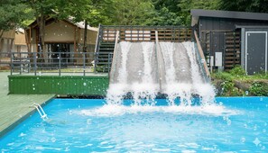 Una piscina con tobogán, rodeada por un muelle de madera y una valla.