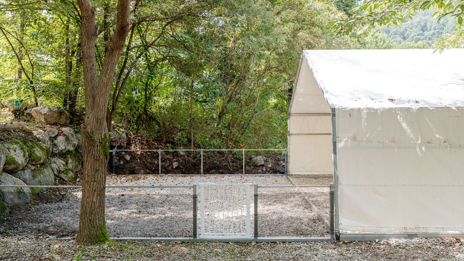A covered outdoor area with a gravel path, a metal fence, and a building with a white roof.