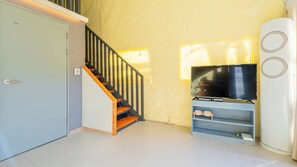 Een kamer met een trap, een televisie op een standaard en een wit kastje.