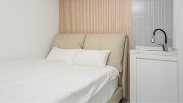 A bed with a headboard, a bedside table, and a wall-mounted sink.