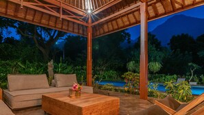 A covered outdoor seating area with a pool, wooden furniture, and lush greenery. - Luxury Living in Harmony with Nature! (bali)