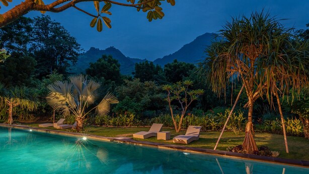 A poolside area with lounge chairs and a well-maintained lawn, surrounded by tropical plants and a mountainous backdrop. - Luxury Living in Harmony with Nature! (bali)