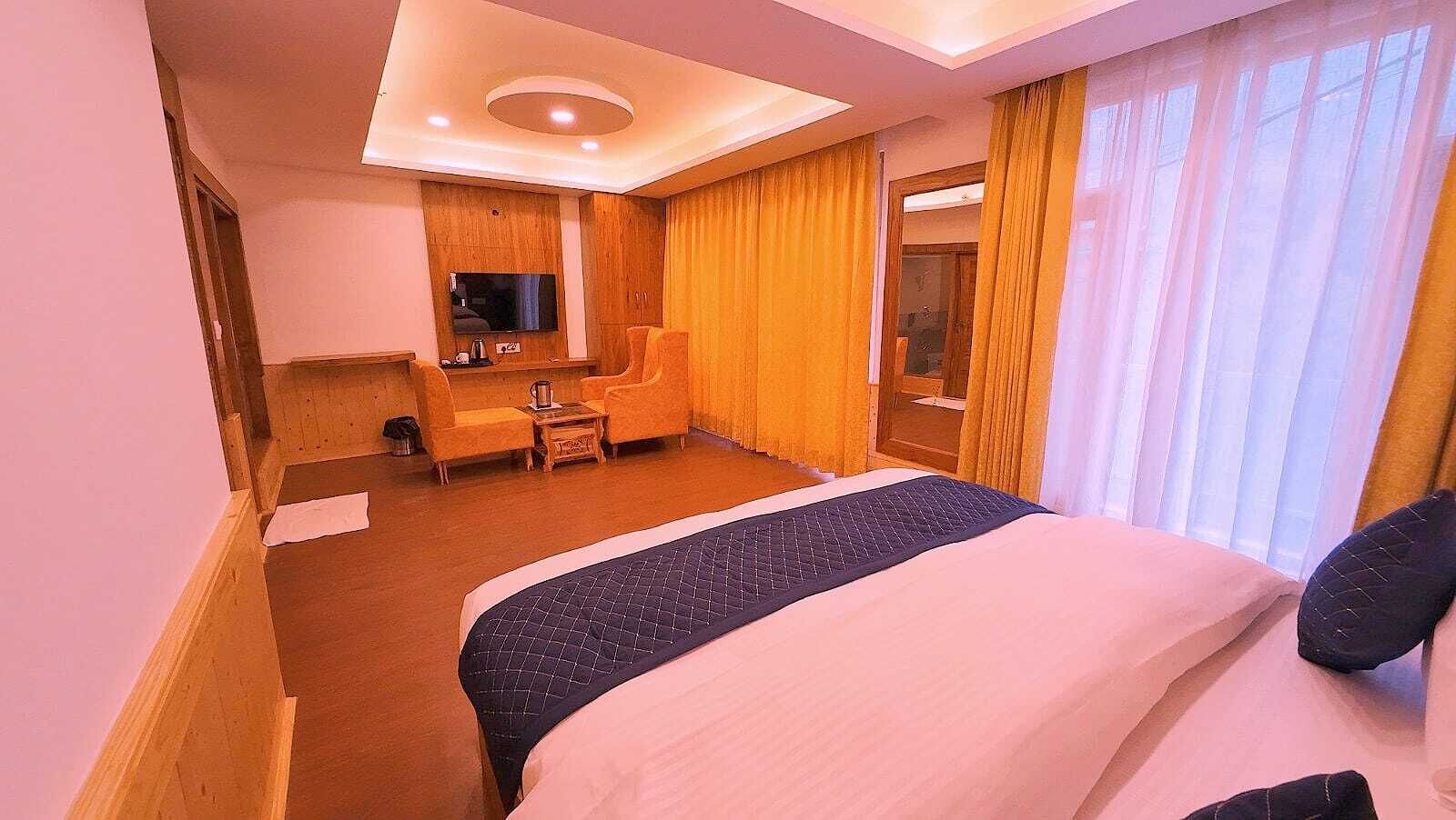 Ein Hotelzimmer mit einem großen Bett, einem Schreibtisch mit Stuhl, einem Fernseher und einem Fenster mit Vorhängen.