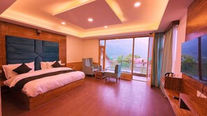 A modern bedroom with a large bed, a desk, and a chair, featuring a view of the mountains through large windows.