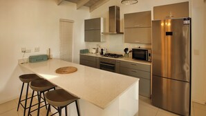 A modern kitchen with a central island, bar stools, stainless steel appliances, and a large refrigerator. - La Maison, Langebaan 6-sleeper (Langebaan)