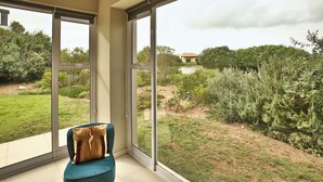 A room with large windows offering a view of a landscaped garden and a distant building. - La Maison, Langebaan 6-sleeper (Langebaan)