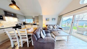 A modern kitchen with white cabinets, a dining table with chairs, a sofa, and a large window with a view of a backyard. - Badger's Retreat -  a beach house that sleeps 4 guests  in 2 bedrooms (Filey)