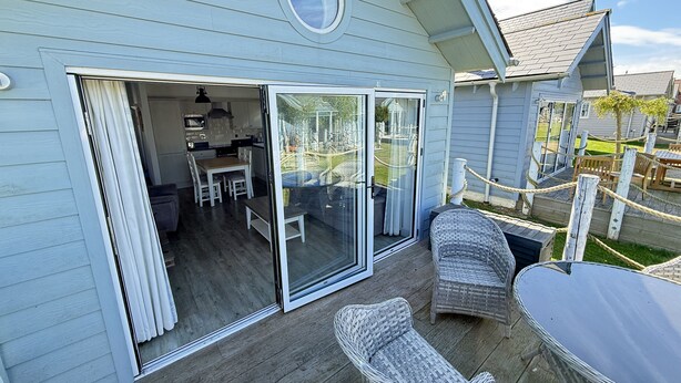 A covered deck with wicker furniture, a dining area, and a sliding glass door leading to a kitchen. - Badger's Retreat -  a beach house that sleeps 4 guests  in 2 bedrooms (Filey)