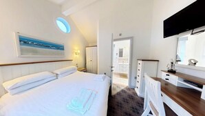 A hotel room with a bed, a desk with a mirror, a television, a painting, and a door leading to a bathroom. - Badger's Retreat -  a beach house that sleeps 4 guests  in 2 bedrooms (Filey)