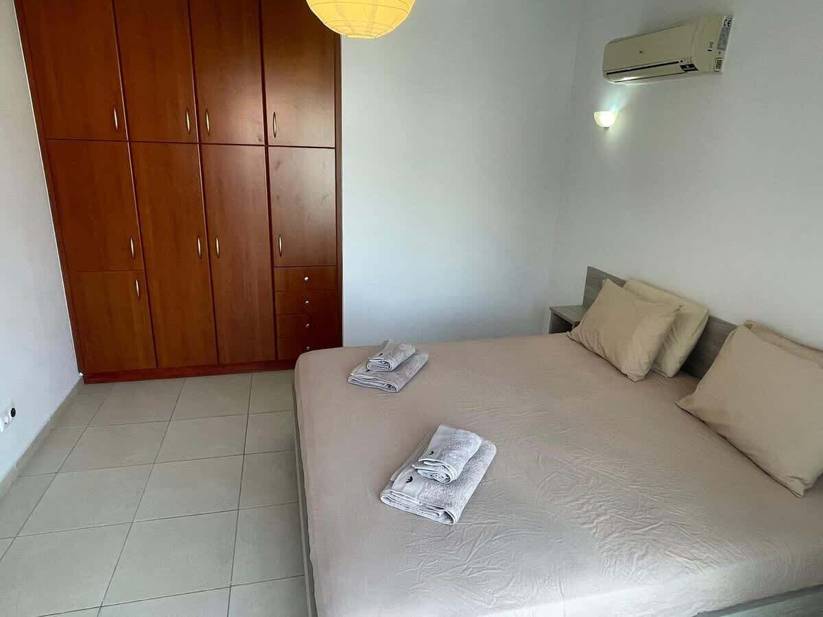 A bedroom with a bed, two pillows, a wardrobe, and an air conditioning unit.