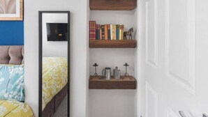 A bedroom with a bed, a bedside table, a mirror, and a shelf with books and a small figurine. - OnSiteStays - Rose Cottage: Cozy Lewes Getaway (Barcombe)