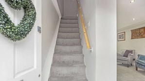 A staircase with a wooden handrail, carpeted steps, and a green wreath on the wall. - OnSiteStays - Rose Cottage: Cozy Lewes Getaway (Barcombe)